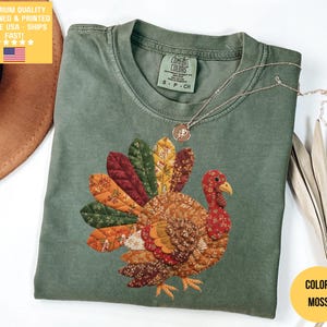 May include: A moss green t-shirt featuring a colorful turkey design. The turkey has a patchwork-style design with various patterns and colors. The shirt has a crew neck and short sleeves. The text "PREMIUM QUALITY DESIGNED & PRINTED IN THE USA - SHIPS FAST!" is visible.