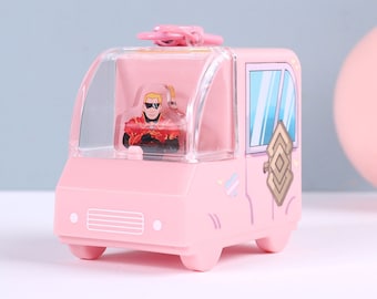 May include: A pink toy van with a clear windshield and a small figure of a person inside. The van has decorative elements on the side and a pink sphere is next to it. The background has blue and yellow shapes.