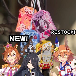 May include: Four rectangular fabric omamori charms featuring embroidered anime-style character illustrations in orange, purple, blue, and yellow. The charms have decorative knotted cords at the top. Text overlays read NEW! and RESTOCK!