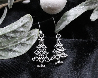 May include: A pair of silver tone earrings shaped like Christmas trees. The earrings are hanging from a black background.