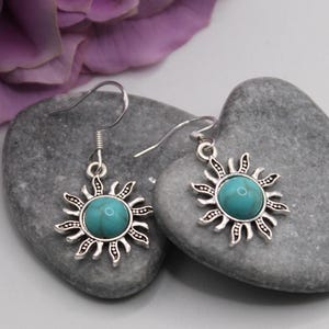 May include: A pair of silver dangle earrings with turquoise stones set in a sunburst design.