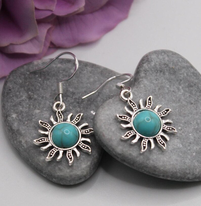 May include: A pair of silver dangle earrings with turquoise stones set in a sunburst design.