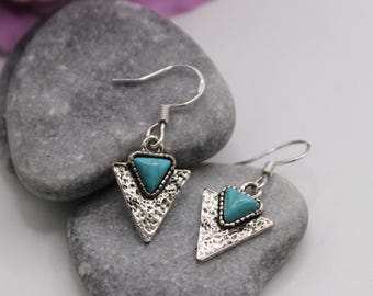 May include: A pair of silver triangle earrings with turquoise stones. The earrings have a textured, hammered look.