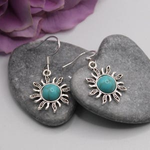 May include: A pair of silver dangle earrings with turquoise sun charms. The earrings have a simple hook closure.