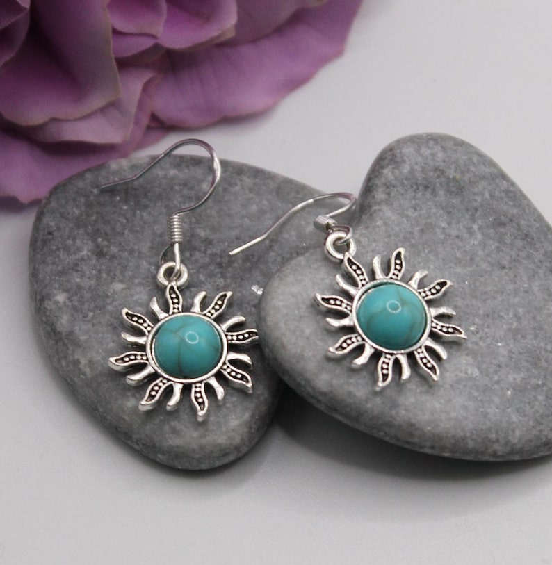 May include: A pair of silver dangle earrings with turquoise sun charms. The earrings have a simple hook closure.