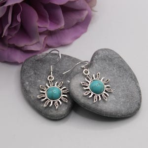 May include: A pair of silver earrings with turquoise stones in the center of a sun design.