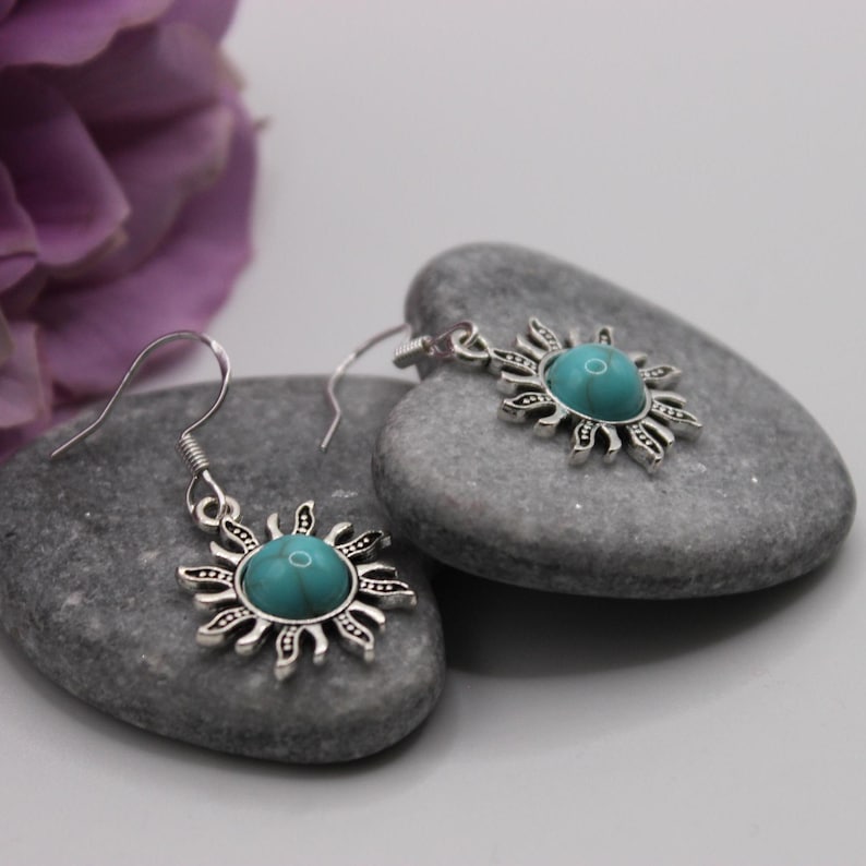 May include: A pair of silver earrings with turquoise stones set in a sunburst design. The earrings are hanging from silver hooks.