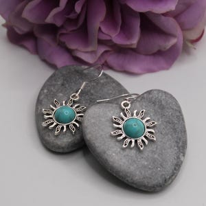 May include: Silver earrings with turquoise stones in the center of a sun design.