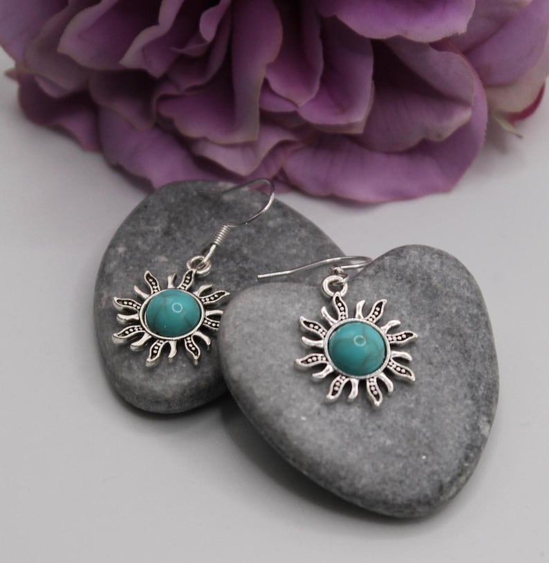 May include: Silver earrings with turquoise stones in the center of a sun design.