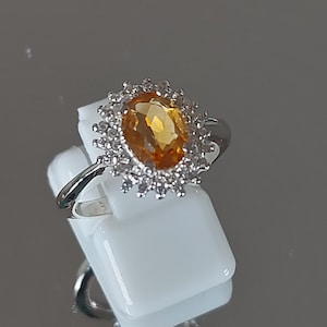 Peut inclure: Une bague en argent avec une grande topaze ovale entourée de petites pierres précieuses claires.