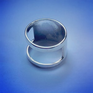 Può includere: Un anello d'argento con una fascia larga e un design a taglio. L'anello è aperto da un lato, creando un look unico e moderno.