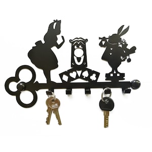 Puede incluir: Porta llaves de metal negro con forma de llave con personajes de Alicia en el País de las Maravillas, incluyendo a Alicia, el Conejo Blanco y el Sombrerero Loco. Tiene cinco ganchos para colgar llaves.