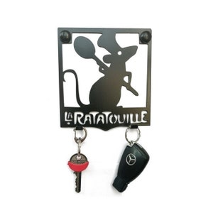 May include: Black metal key holder with a rat chef silhouette holding a spoon, and the text "LA RATATOUILLE". Two keys hang from the holder. The key holder is mounted on a white background.