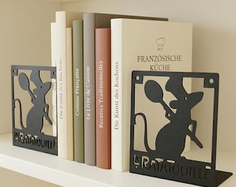 May include: A pair of black metal bookends featuring a cutout silhouette of a mouse wearing a chef hat and holding a spoon, with the word Ratatouille cut out at the base, supporting a row of books with titles like Französische Küche.