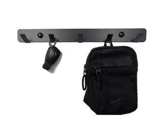 May include: Black metal wall mounted hook rack with five hooks. A black bag with a white logo is hanging on one of the hooks. A black key chain with a silver key is hanging on another hook.