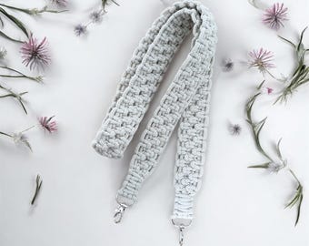 May include: A white crocheted strap with silver metal clasps. The strap is made of a thick, textured yarn and is perfect for a bag or purse.
