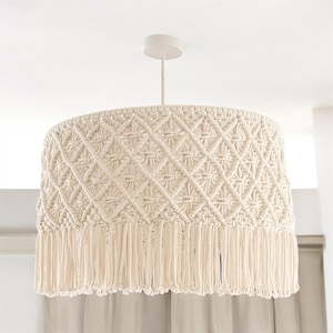 May include: A white macrame pendant light fixture with a fringe trim. The light fixture has a diamond pattern.