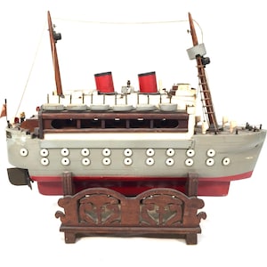May include: A vintage wooden model of a passenger ship with red accents, white portholes, and a wooden stand.