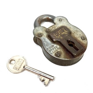 May include: An antique, weathered padlock with a matching key. The padlock is a tarnished silver color with a brown keyhole cover and the text "FOUR BRASS LEVERS". The key is silver with the text "SQUIRE".