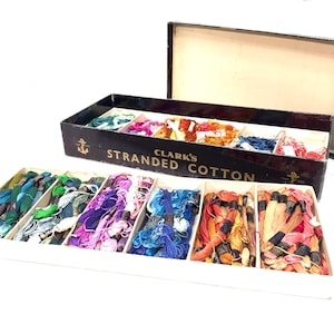 May include: A vintage box of Clark's Stranded Cotton embroidery floss. The box is black with gold lettering and an anchor design. The floss is arranged in rows of different colors, including green, blue, pink, and orange.