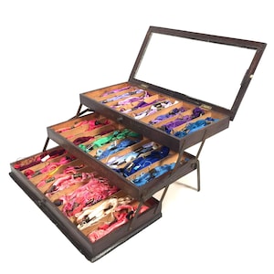 May include: A vintage wooden thread organizer with three tiered drawers, each filled with colorful embroidery floss. The top tier has a glass lid. The floss colors include pinks, blues, greens, and purples. The organizer is open, displaying the contents.
