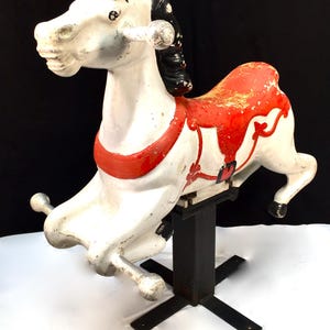 May include: A vintage carousel horse, painted white with red and black details. The horse is mounted on a black metal stand with a square base.