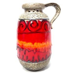 May include: A vintage ceramic pitcher with a handle. The pitcher features a vibrant color scheme of red, orange, and brown. The top and base are a speckled gray. Black swirl designs adorn the red body.