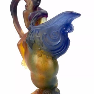 May include: A glass sculpture of a woman riding a winged horse. The sculpture is made of iridescent glass with shades of blue, green, and brown.