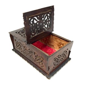 May include: A wooden box with intricate carvings and a red velvet lining. The box has a hinged lid with a cutout design.