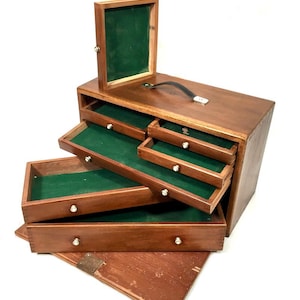 May include: A wooden jewelry box with multiple drawers and a hinged top. The box is stained a warm brown color, with green felt lining the drawers. Each drawer has a small, round silver knob for opening.