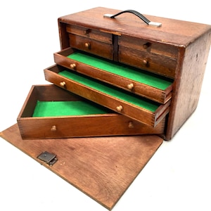 May include: A wooden tool chest with multiple drawers, some open to reveal green felt lining. The chest has a black handle and a hinged lid. The drawers have small, round knobs.
