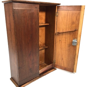 May include: A tall, rectangular wooden wall cabinet with a dark brown finish. The cabinet features one closed door on the left and one open door on the right, revealing two interior shelves and a metal latch. The base displays the text Wolverhampton.