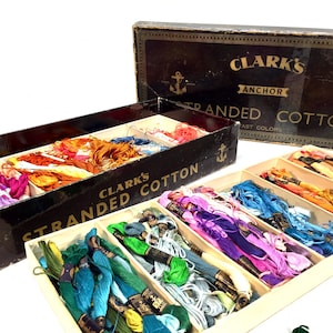 May include: A wooden box filled with spools of colorful stranded cotton thread. The box is labeled "Clark's Anchor Stranded Cotton Fast Colors".