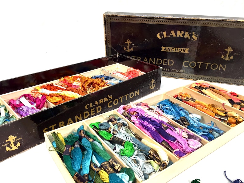 May include: A wooden box filled with spools of colorful stranded cotton thread. The box is labeled "Clark's Anchor Stranded Cotton Fast Colors".