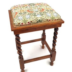 Puede incluir: Un taburete de madera con un cojín cuadrado con estampado floral y patas torneadas.