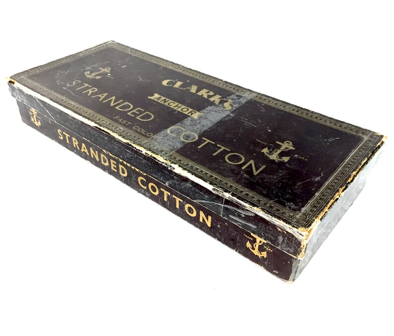 May include: A vintage box of Clark's Anchor Stranded Cotton thread. The box is black with gold lettering and an anchor symbol. The text on the box reads "Clark's Anchor Stranded Cotton Fast Color."