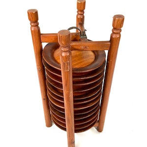 May include: A wooden plate rack with a stack of 10 round wooden plates. The rack is made of dark brown wood and has a metal latch.