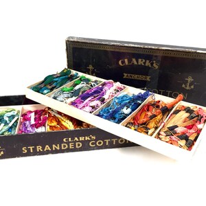 May include: A vintage box of Clark's Anchor Stranded Cotton embroidery floss. The box is black with gold lettering and an anchor design. The box is open, revealing a variety of colors of floss.