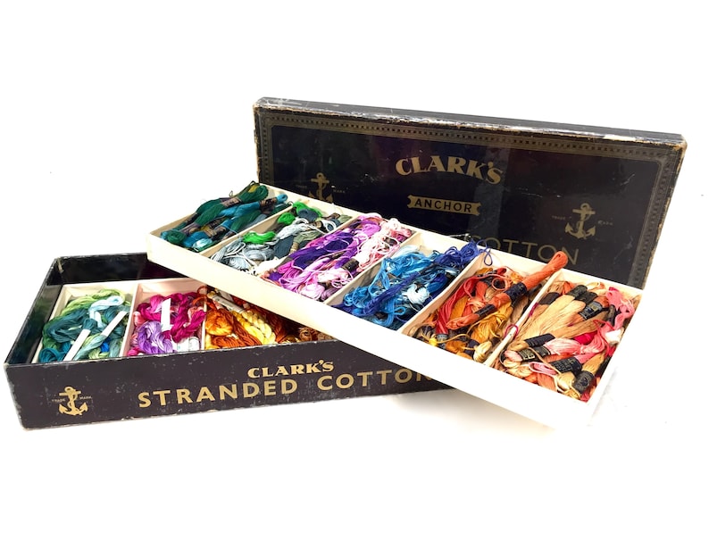 May include: A vintage box of Clark's Anchor Stranded Cotton embroidery floss. The box is black with gold lettering and an anchor design. The box is open, revealing a variety of colors of floss.
