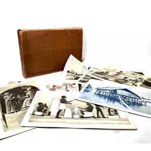 May include: A brown cardboard box containing a set of vintage black and white photographs depicting scenes from ancient Egypt. The photographs are printed on thick paper and have a textured surface. The box is closed and has a simple design.