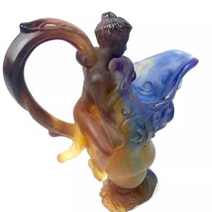 May include: A glass sculpture of a figure riding a mythical creature. The sculpture is made of layered glass in shades of blue, purple, brown, and yellow.