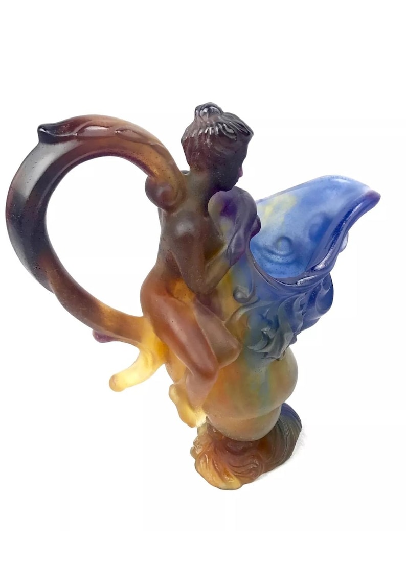 May include: A glass sculpture of a figure riding a mythical creature. The sculpture is made of layered glass in shades of blue, purple, brown, and yellow.