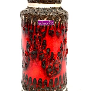 May include: A ceramic vase with a textured, lava-like design. The vase has a vibrant red centre, bordered by dark brown and white bands. The brand name "scheurich" is visible on the front.