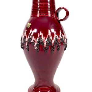 May include: A large, red ceramic vase with a textured, white and black glaze. The vase has a handle and a wide base.