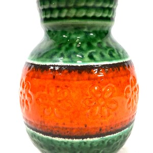 Op de afbeelding: Een groene en oranje keramische vaas met een getextureerd bloemenpatroon. De vaas heeft een brede basis en een smalle hals.