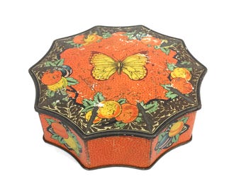 May include: An antique, octagonal tin box with a vibrant orange background and a detailed butterfly illustration. The lid features a yellow butterfly and is surrounded by fruit and foliage. The box has a textured surface and a black border.