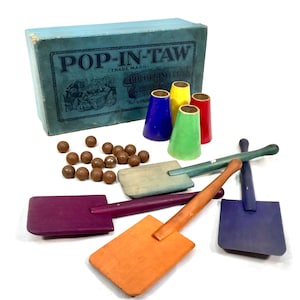 Könnte beinhalten: Vintage Holzspiel Pop-In-Taw in einer blauen Schachtel mit einem bunten Design. Das Spiel enthält Holzschaufeln, Bälle und bunte Kegel.