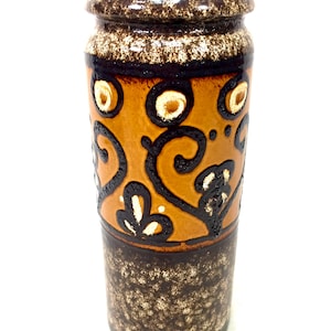 May include: A brown and orange ceramic vase with a floral pattern. The vase has a speckled glaze and a brown rim.