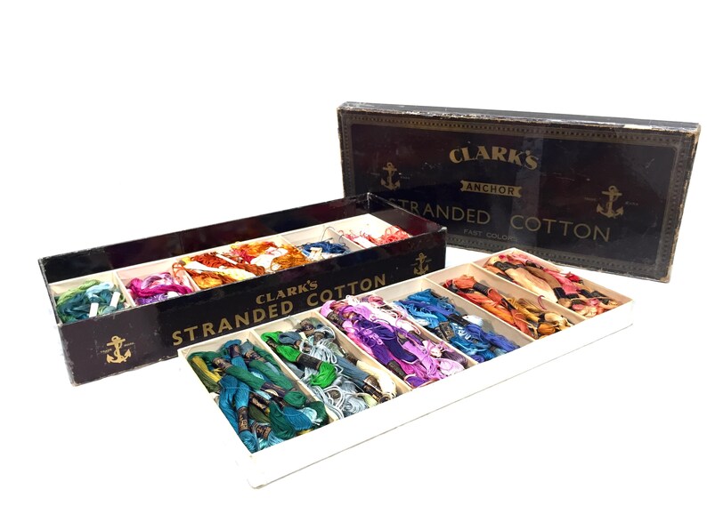 May include: A box of Clark's Anchor Stranded Cotton embroidery floss in a variety of colors. The box is open and the floss is arranged in rows. The box is black with gold lettering and an anchor logo.