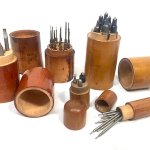 May include: A collection of vintage wooden tool holders, each cylindrical with a natural wood finish. Some contain various metal tools, including screwdrivers and precision bits. The set includes several open containers and lidded cases.